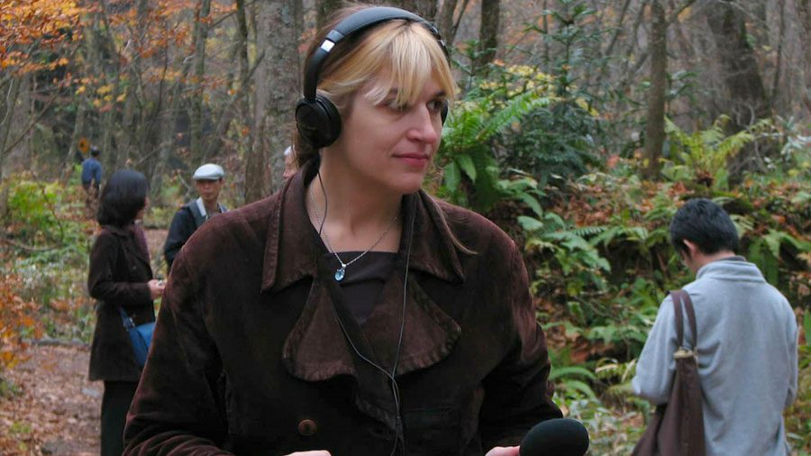 Photo of Andrea Polli wearing headphones holding a microphone in the forest
